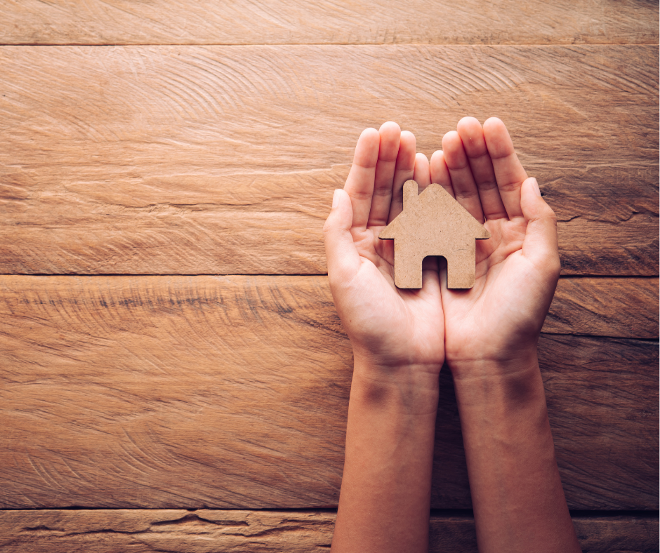 Two hands holding a cutout picture of a house. 